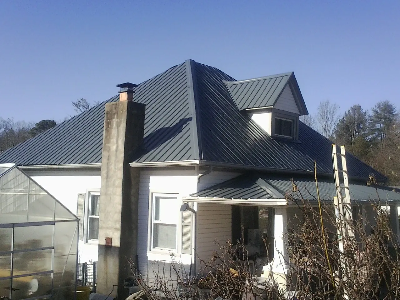 Dark blue standing seam metal roof on a white farmhouse with dormer — Slate & Tile Roof Repair by Roofing Brothers in New Suffolk