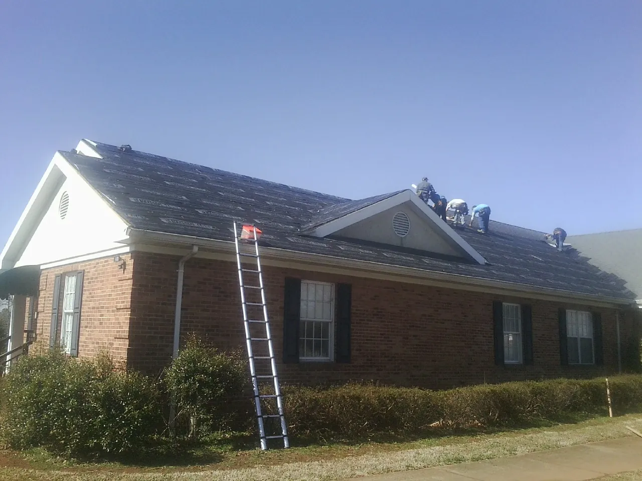 Crew tearing shingles off a brick ranch roof with a ladder set — Metal Roof Repair work by our crew in New Suffolk