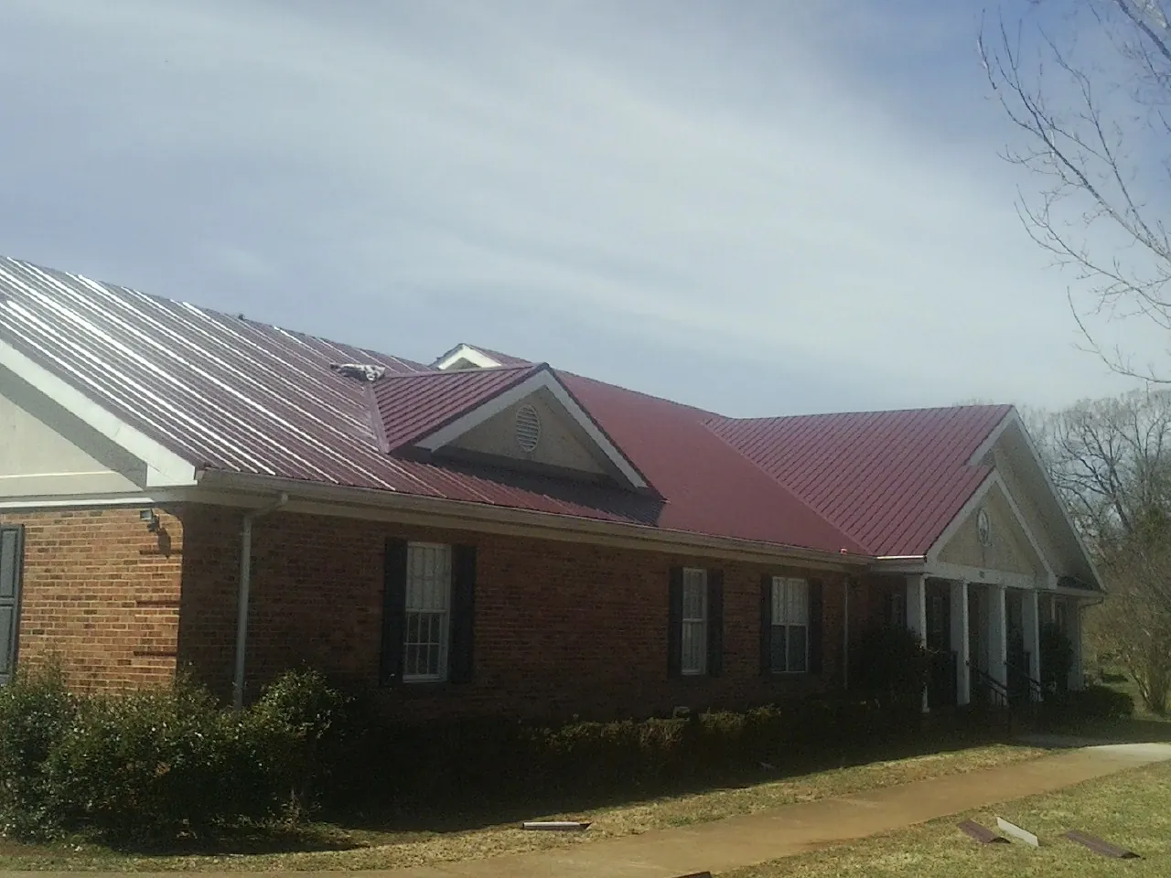 Red metal roof with gabled entries on a long brick building, from a Hail Damage Roof Repair job in New Suffolk
