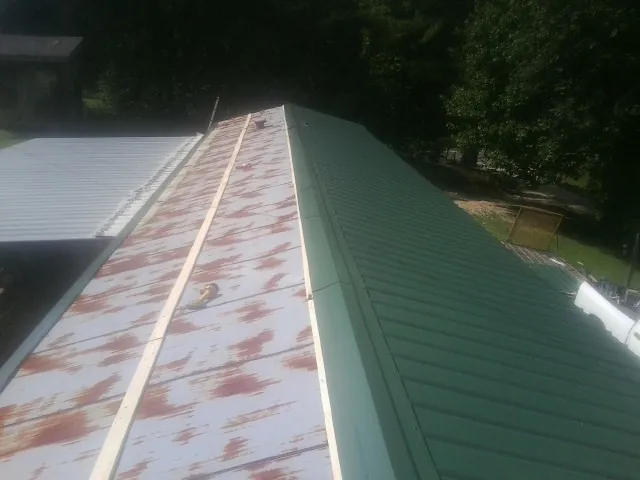 Old rusted panels beside newly installed green metal roofing — Wind Damage Roof Repair by Roofing Brothers in New Suffolk