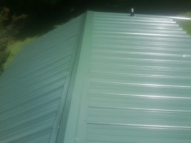 New green metal panels meeting at the ridge of a roof — Flat Roof Repair work by our crew in New Suffolk