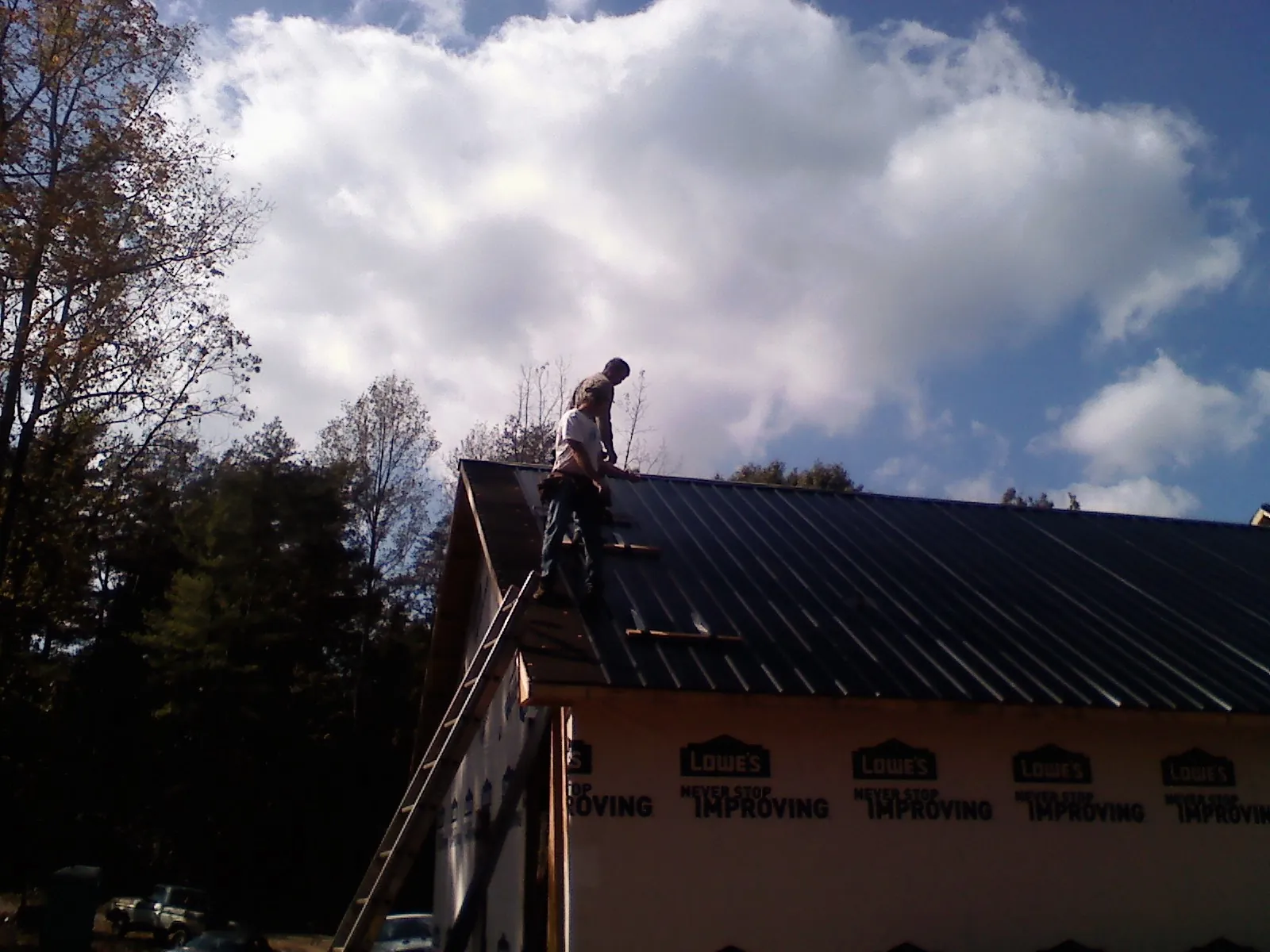 Roofer fastening dark metal panels high against a cloudy sky, from a Roof Inspection job in New Suffolk