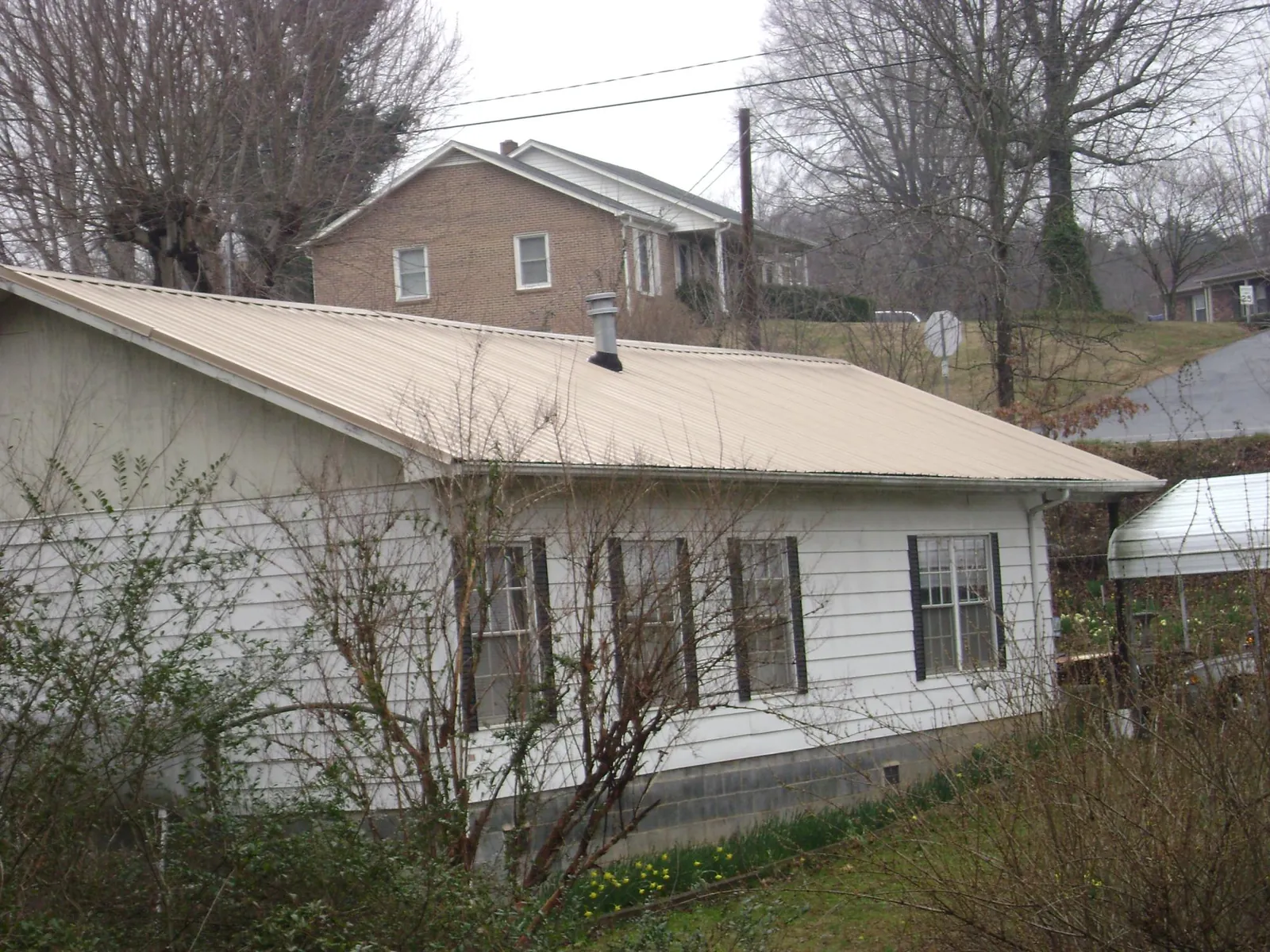 Tan metal roof on a white sided house set into a hillside — Commercial Roofing by Roofing Brothers in New Suffolk